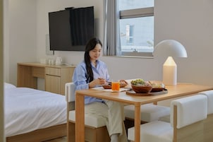Habitación de hotel con cama, escritorio con televisor de pantalla plana, mesa de comedor con lámpara y ventana con cortinas.