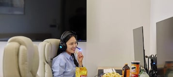 Una persona en una habitación de hotel con escritorio, auriculares, aperitivos y una computadora.