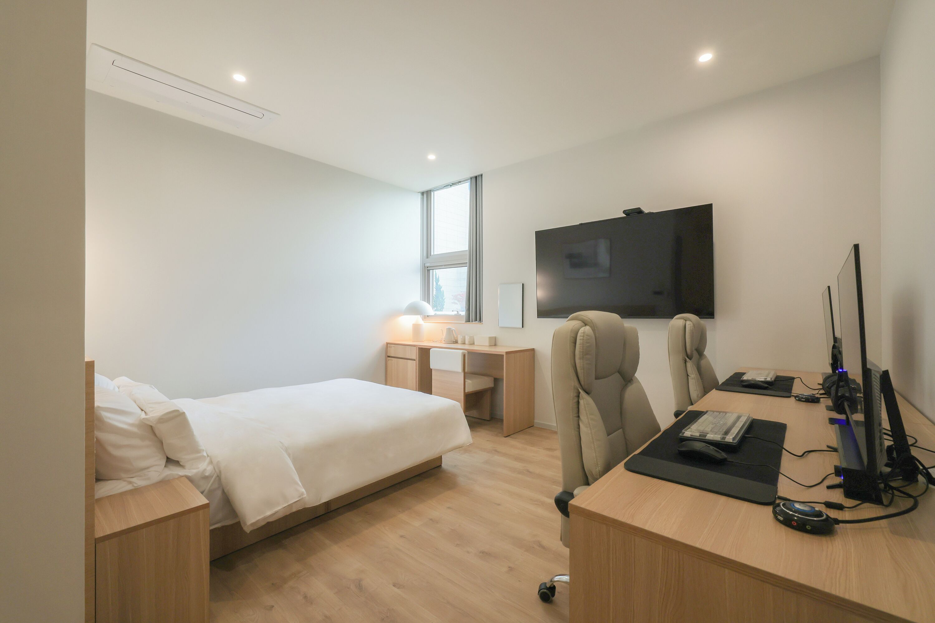 Quarto de hotel moderno com cama, escrivaninha, cadeira, computador e TV.