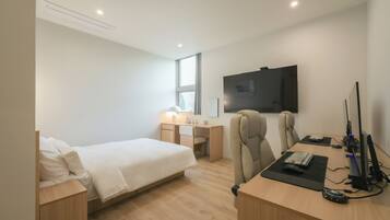 Quarto de hotel moderno com cama, escrivaninha, cadeira, computador e TV.