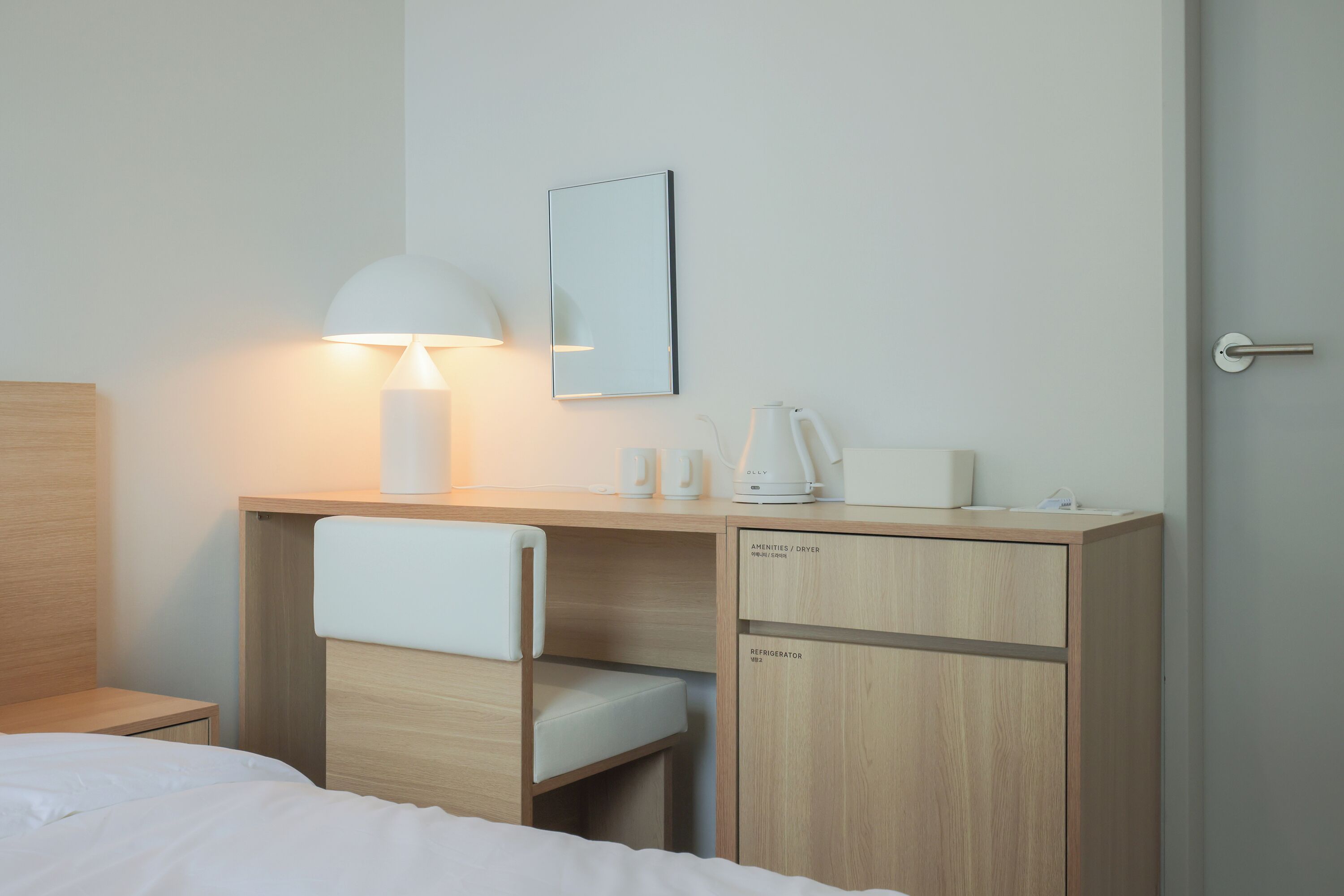 Habitación de hotel con cama, escritorio con lámpara, espejo, cafetera y minibar.