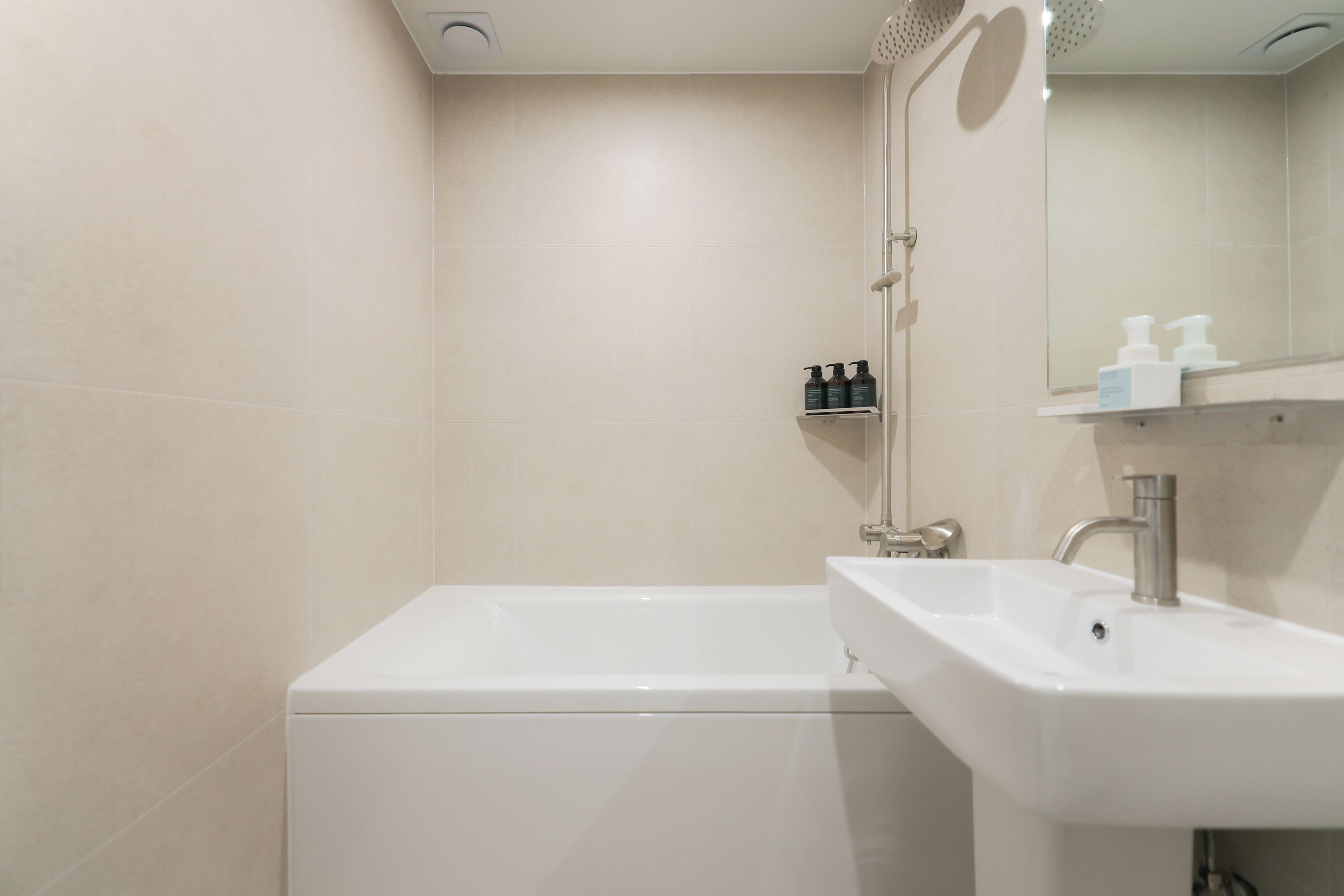A modern bathroom with a white bathtub, a sink, and a mirror. There are toiletries on a shelf.