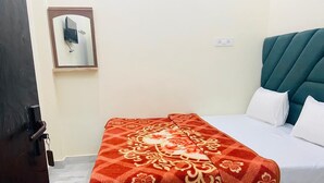 Een hotelkamer met een bed, een rode bedspreide met patroon, witte kussens, een donker hoofdbord en een tv aan de muur.