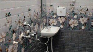 Een badkamer met een douche, wastafel en toilet. De wandtegels hebben een bloemenmotief.