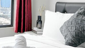 Un letto rifatto con lenzuola bianche, un cuscino grigio con texture e un asciugamano bianco piegato sul letto.