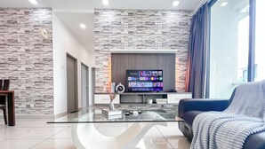 Un soggiorno moderno con parete in pietra, tavolino in vetro, divano blu e televisore a schermo piatto che mostra l'interfaccia di una piattaforma di streaming.