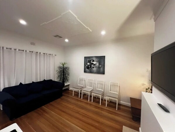 A modern living room with a dark-colored sofa, a white chair arrangement, a potted plant, and a black and white artwork on the wall.