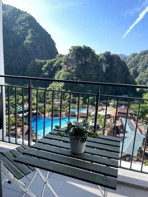 Enjoy breathtaking views of the surrounding mountains from this balcony, overlooking a serene pool area with a soothing waterfall.