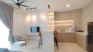 A modern living room with a sofa, a coffee table, and a TV. There is a kitchen area with a dining table and chairs. - IPOH Sunway Onsen Suites by uBook (Ipoh)