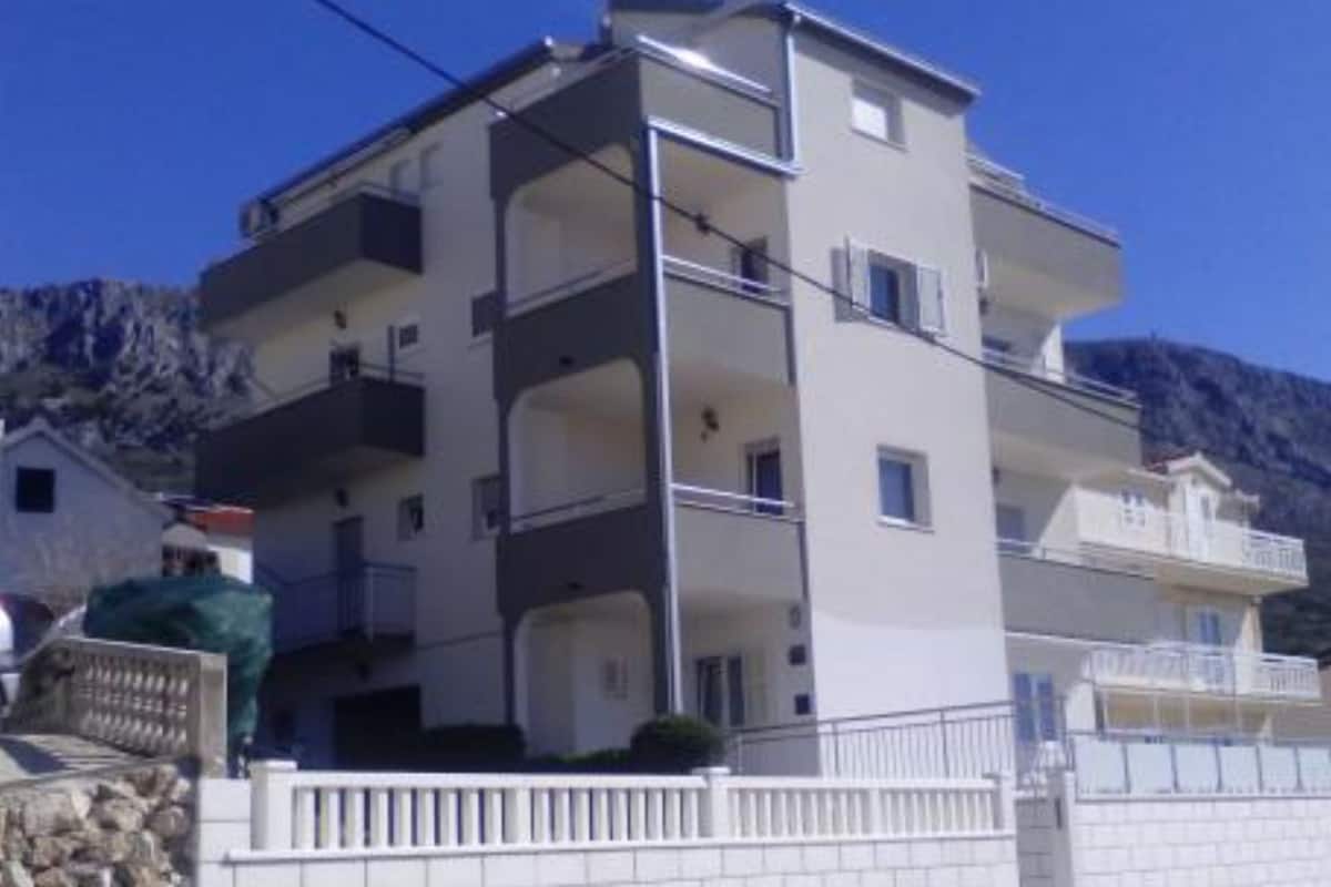 A multi-story residential building with balconies, a stone wall, and a clear view of the surrounding mountains.
