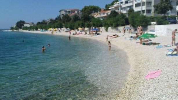 A beach with clear water, people swimming and sunbathing, and buildings in the background. - Apartments Cihorich (Dugi Rat)