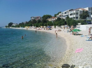 A beach with clear water, people swimming and sunbathing, and buildings in the background. - Apartments Cihorich (Dugi Rat)