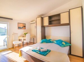 Ein Schlafzimmer mit einem Bett, einem Schreibtisch und einem Stuhl. An der Wand hängt ein Bild und über dem Schreibtisch befindet sich eine Klimaanlage.