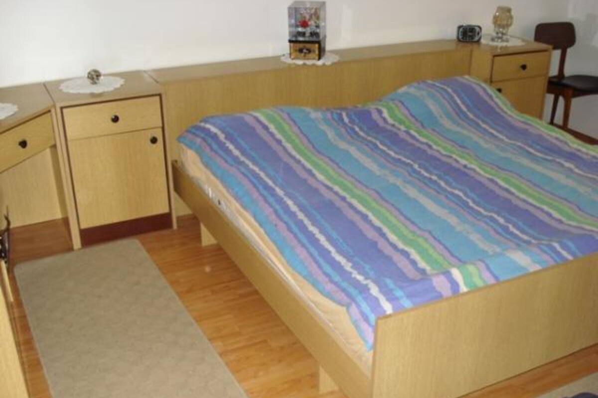 A bedroom with a wooden bed, a nightstand, a dresser, and a small table with a radio.