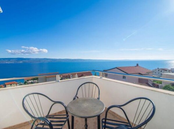 A balcony with a table and chairs overlooking a coastal view. - Apartments Cihorich (Dugi Rat)