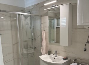 Ein modernes Badezimmer mit einer Duschkabine aus Glas, einem weißen Waschbecken und einem Spiegel darüber.