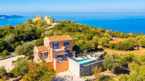 En villa i middelhavsstil med pool, omgivet af frodig vegetation med udsigt over havet.