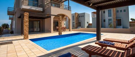 A modern pool area with a clear blue pool, wooden lounge chairs, and a covered seating area.