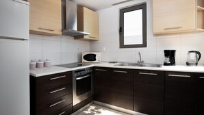 A modern kitchen with dark wooden cabinets, a white countertop, a built-in microwave, a stove, and a coffee maker. - Villa Blue Wave Tessera (Rhodes)