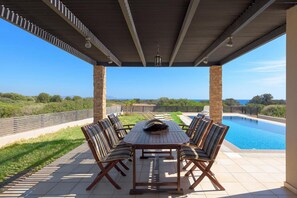 Eine Terrasse im Freien mit Tisch und Stühlen, ein Schwimmbecken und eine Landschafts Aussicht.