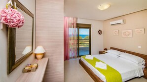 A hotel room with a bed, a bedside table with a lamp, a mirror, a window with curtains, and a view of the sea. - Villa Blue Wave Tria (Rhodes)