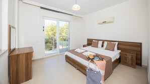 A modern bedroom with a large bed, a wooden nightstand, a bedside table, and a sliding glass door leading to a balcony. - Four Seasons Villa in Oludeniz (Fethiye)