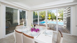 A dining area with a table set for six, large sliding glass doors leading to a pool area. - Four Seasons Villa in Oludeniz (Fethiye)
