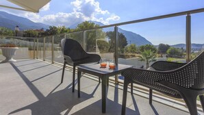 Un balcon doté d’une balustrade en verre, de deux chaises, d’une table et d’une plante en pot.