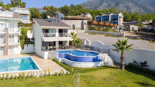 Un quartier résidentiel moderne doté d’une piscine, de plusieurs maisons et bordé par un paysage montagneux.