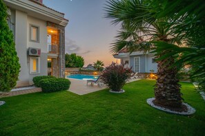 A two-story building with a stone facade, a swimming pool, and a well-maintained lawn with palm trees. - Golden Heights 15 in Oludeniz (Fethiye)