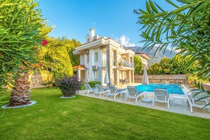 A two-story house with a swimming pool, surrounded by a well-maintained garden and a mountain backdrop. - Golden Heights 15 in Oludeniz (Fethiye)