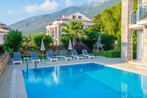 A swimming pool with lounge chairs, a stone wall, and a mountain backdrop. - Golden Heights 15 in Oludeniz (Fethiye)