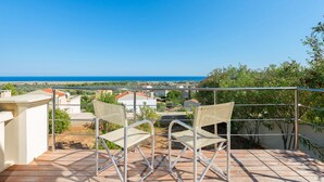 A terrace with two wicker chairs and a metal table, overlooking a coastal landscape with houses and a clear blue sky. - Villa Elena in Kalathos (Rhodes)