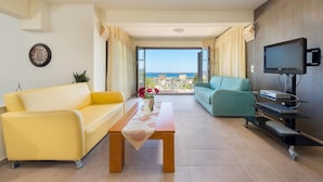 A modern living room with a yellow sofa, a teal sofa, and a wooden coffee table. A flat-screen TV is mounted on the wall, and a balcony with a view of the sea is visible. - Villa Elena in Kalathos (Rhodes)