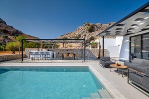 A modern outdoor pool area with a pergola, seating, and a view of rocky hills. - Villa 13 Zendo in Kolympia (Rhodes)