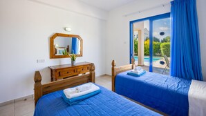 A bedroom with two beds, a wooden dresser, a mirror, and a view of a pool. - Villa Apollonas in Peyia (Pegeia)