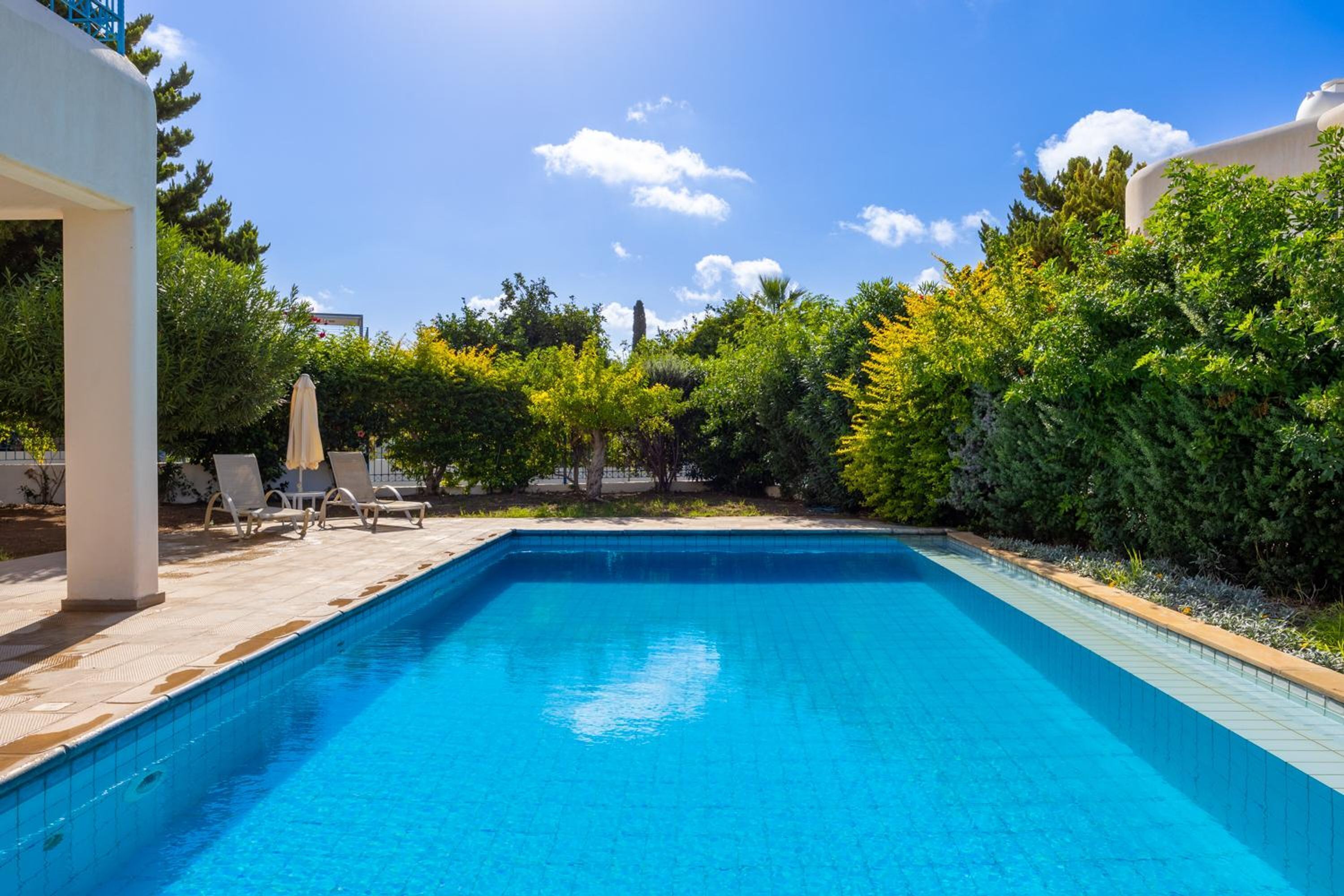 Ein rechteckiger Swimmingpool mit einer gefliesten Kante, umgeben von einer gefliesten Liegefläche und Liegestühlen.