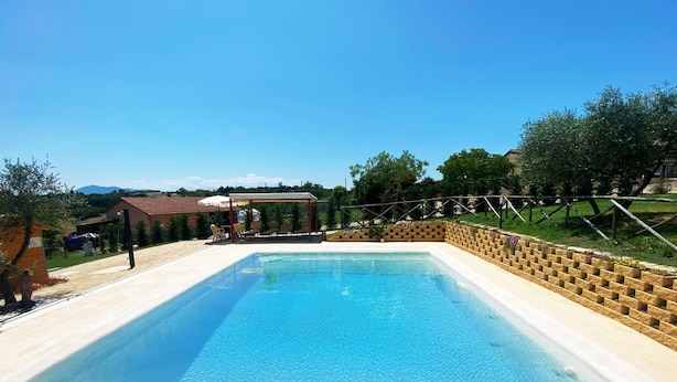A rectangular swimming pool with a tiled deck, surrounded by a brick wall and a wooden fence.