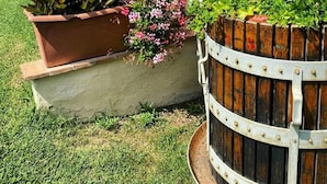 A stone building with a wooden pergola, a bird feeder, and a flower bed with pink flowers.
