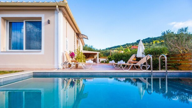 Una piscina con sillones de descanso y sombrillas, una zona de estar cubierta y vistas a una colina.