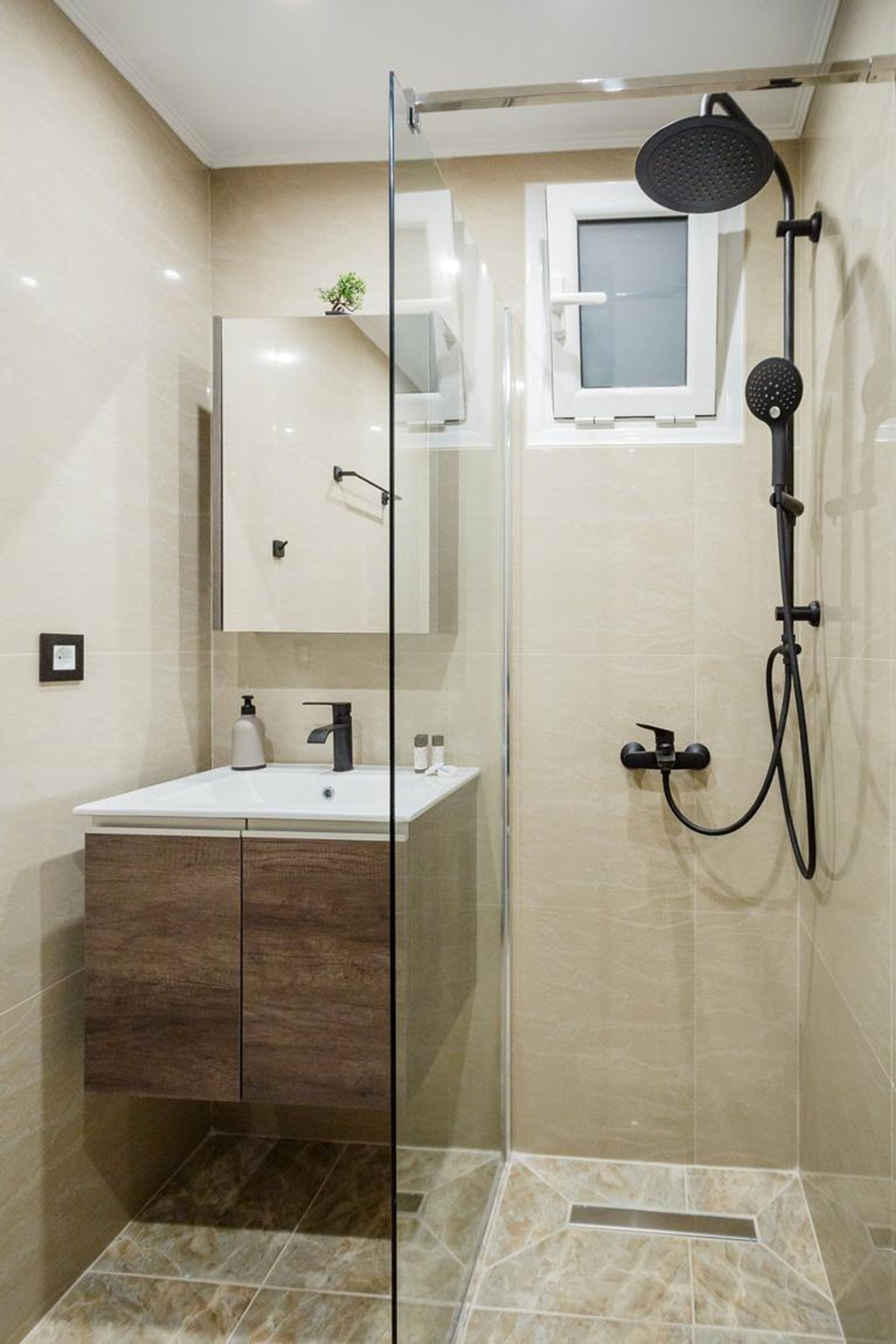 A modern bathroom with a glass shower enclosure, a white sink, and a small window above the mirror.