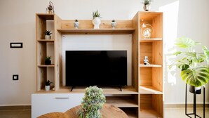 Una sala de estar moderna con un televisor de pantalla plana centrado en un mueble de madera, flanqueado por estantes con objetos decorativos y plantas.