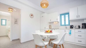A modern kitchen with white cabinets, a round dining table with four chairs, and a fruit bowl on the table. - Villa Kalathos Dream White (Rhodes)