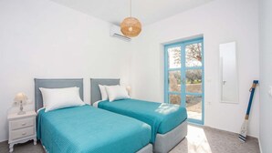 A bedroom with two beds, a nightstand, a window with a view, and a broom leaning against the wall. - Villa Kalathos Dream White (Rhodes)