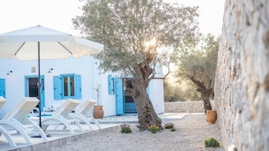 A white building with blue shutters, a large umbrella, and lounge chairs. - Villa Kalathos Dream White (Rhodes)