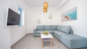 A modern living room with a light blue sectional sofa, a white coffee table, and a painting of boats on the wall. - Villa Kalathos Dream White (Rhodes)