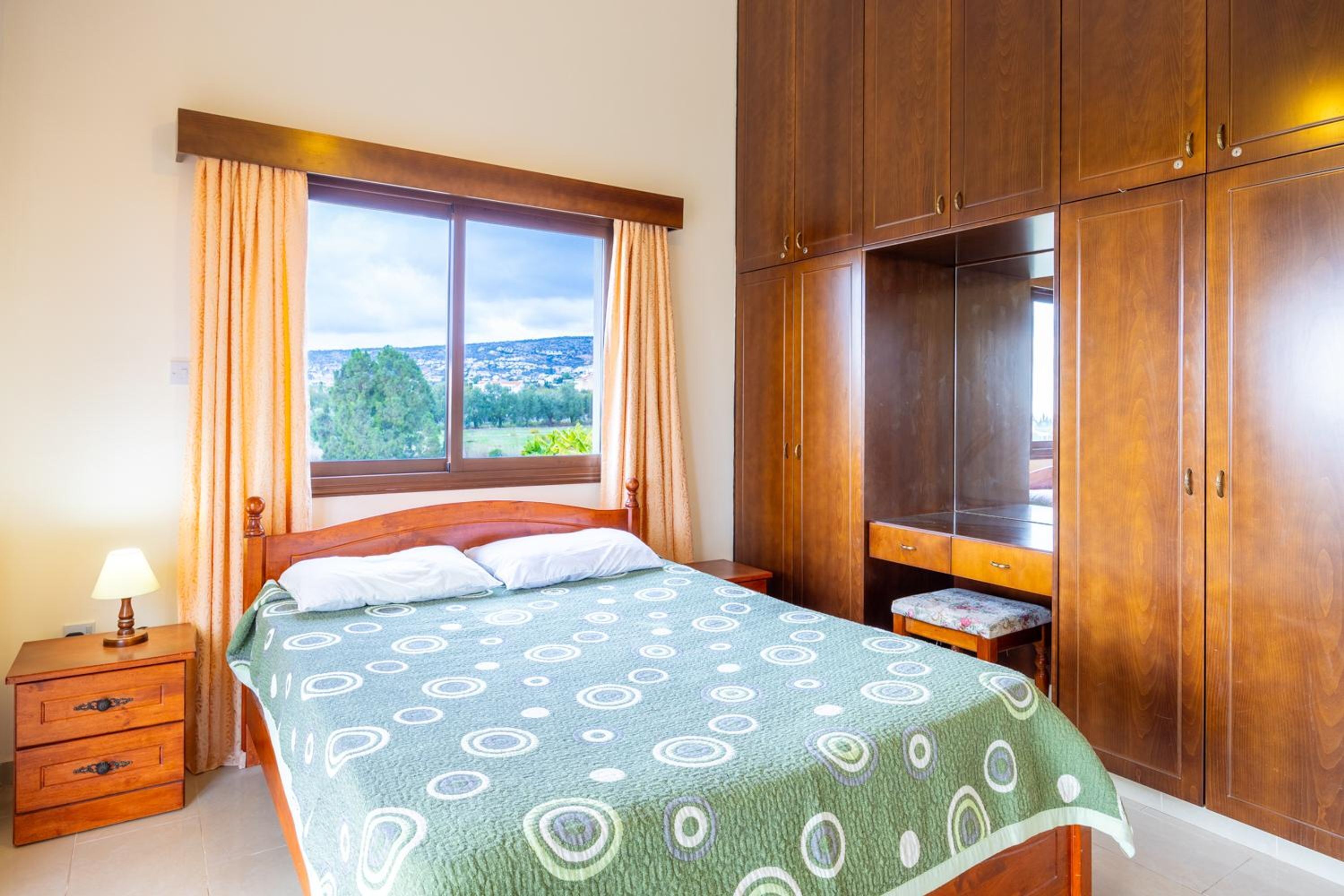 A bedroom with a bed, a nightstand, a wooden wardrobe, and a window with curtains.