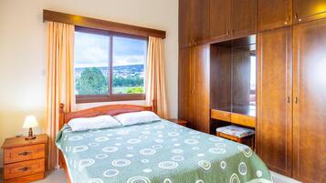 A bedroom with a bed, a nightstand, a wooden wardrobe, and a window with curtains.