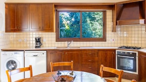 Egy konyha, melyben fa szekrények, mosógép, tűzhely és egy ablak található, ahonnan fákra nyílik kilátás.