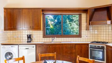A kitchen with wooden cabinets, a washing machine, a stove, and a window with a view of trees.